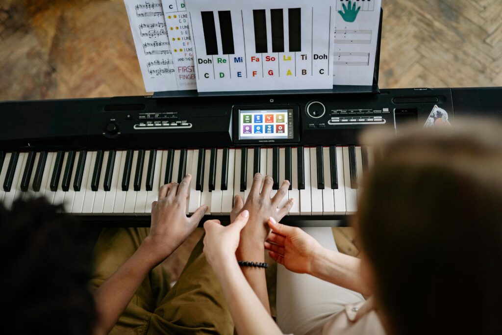 A woman guides a student's hands on a keyboard piano, emphasizing musical instruction.